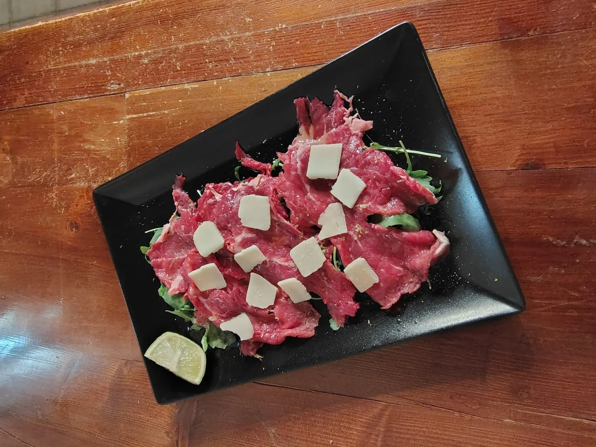 Carpaccio di Wagyu su vassoio nero con rucola, scaglie di parmigiano e limone