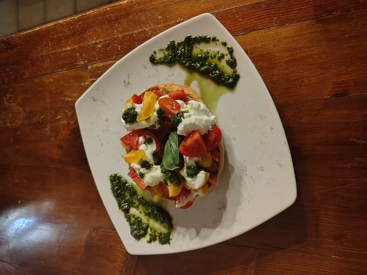 Frisella con burrata, pomodorini colorati e pesto — vista dall'alto su piatto bianco