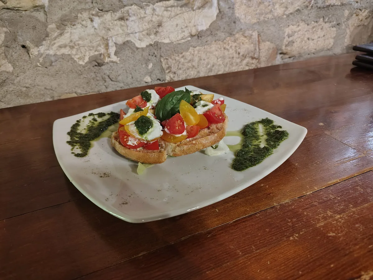 Frisella con mozzarella e pomodorini colorati su piatto grigio — pareti in pietra antica sullo sfondo
