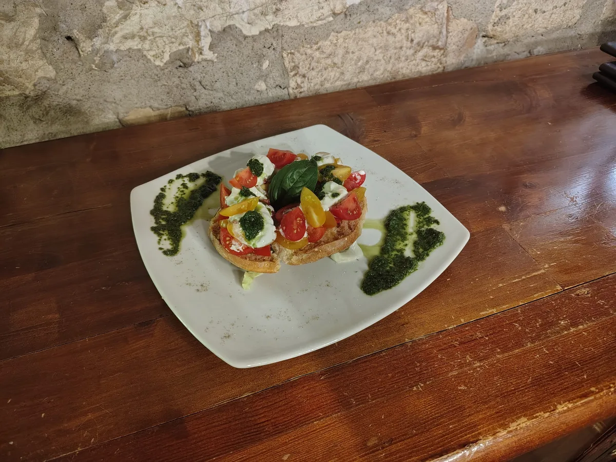 Frisella con stracciatella, pomodorini e basilico su tavolo di legno scuro