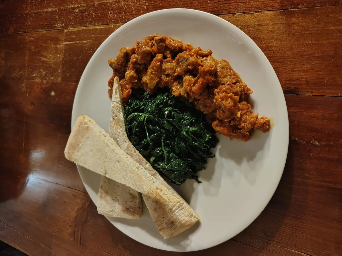 Secondo di guanciale brasato con spinaci saltati e crostini su piatto bianco