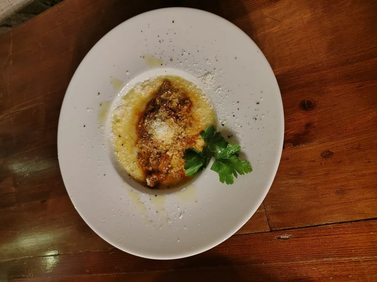 Polenta cremosa con ragù di carne su piatto bianco — piatto del giorno alla Grotta dei Priori