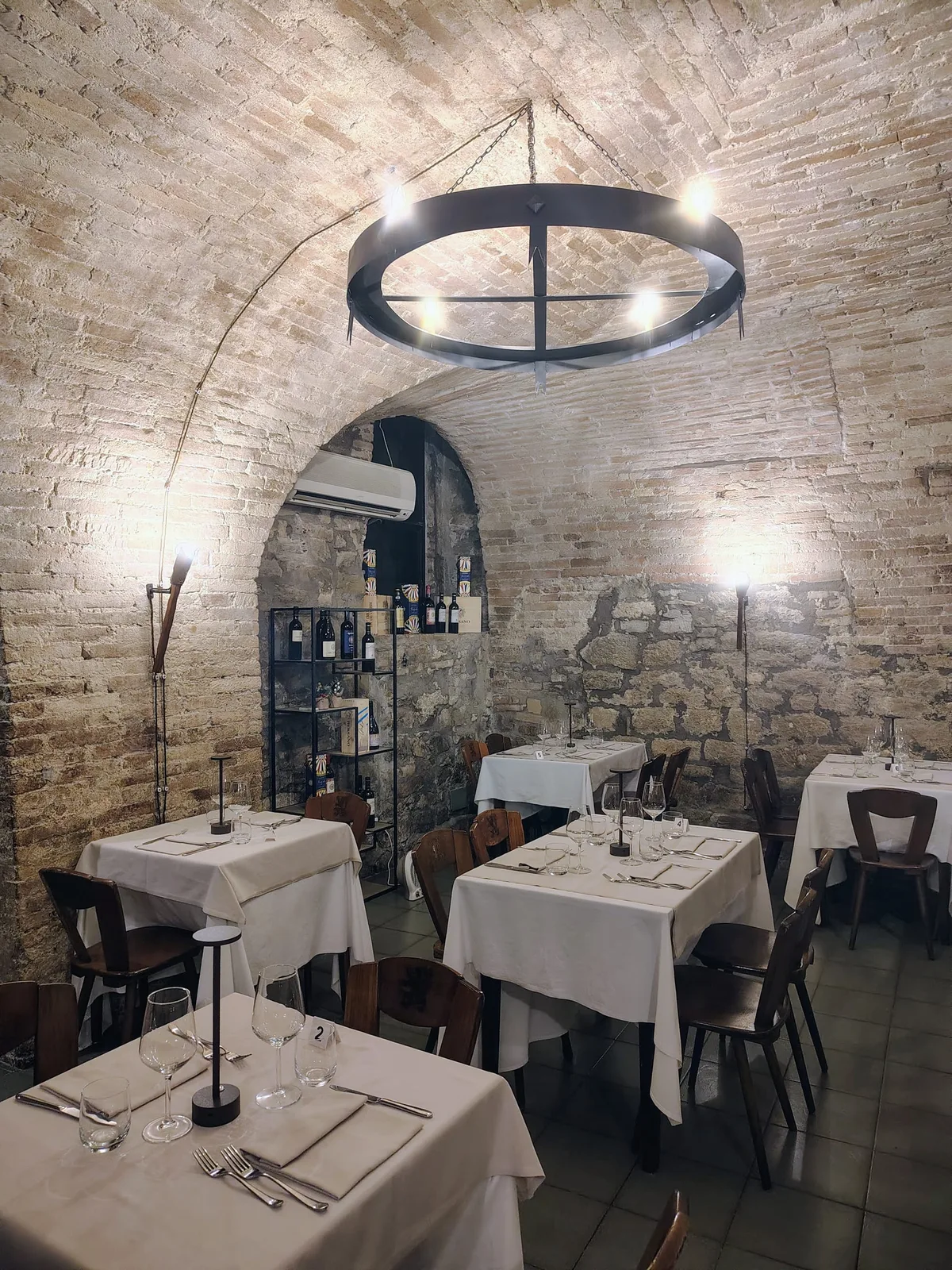 Sala principale con lampadario in ferro, archi in mattoni e tavoli apparecchiati