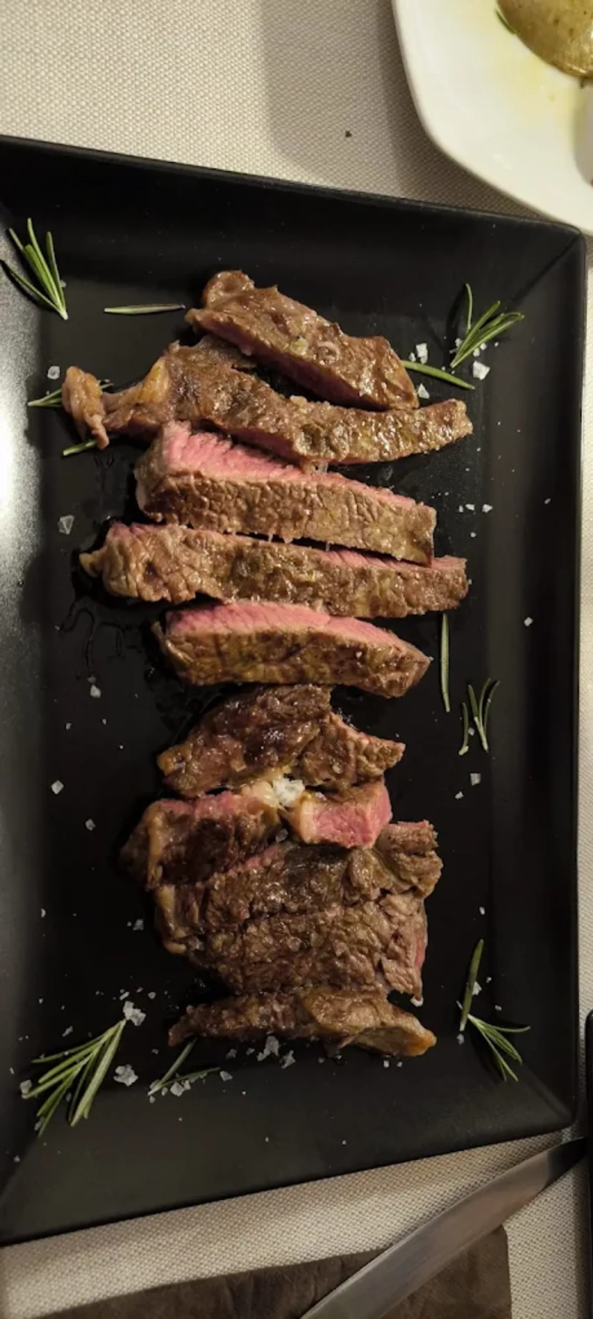 Fette di tagliata di manzo rosé con rosmarino e sale grosso su vassoio nero