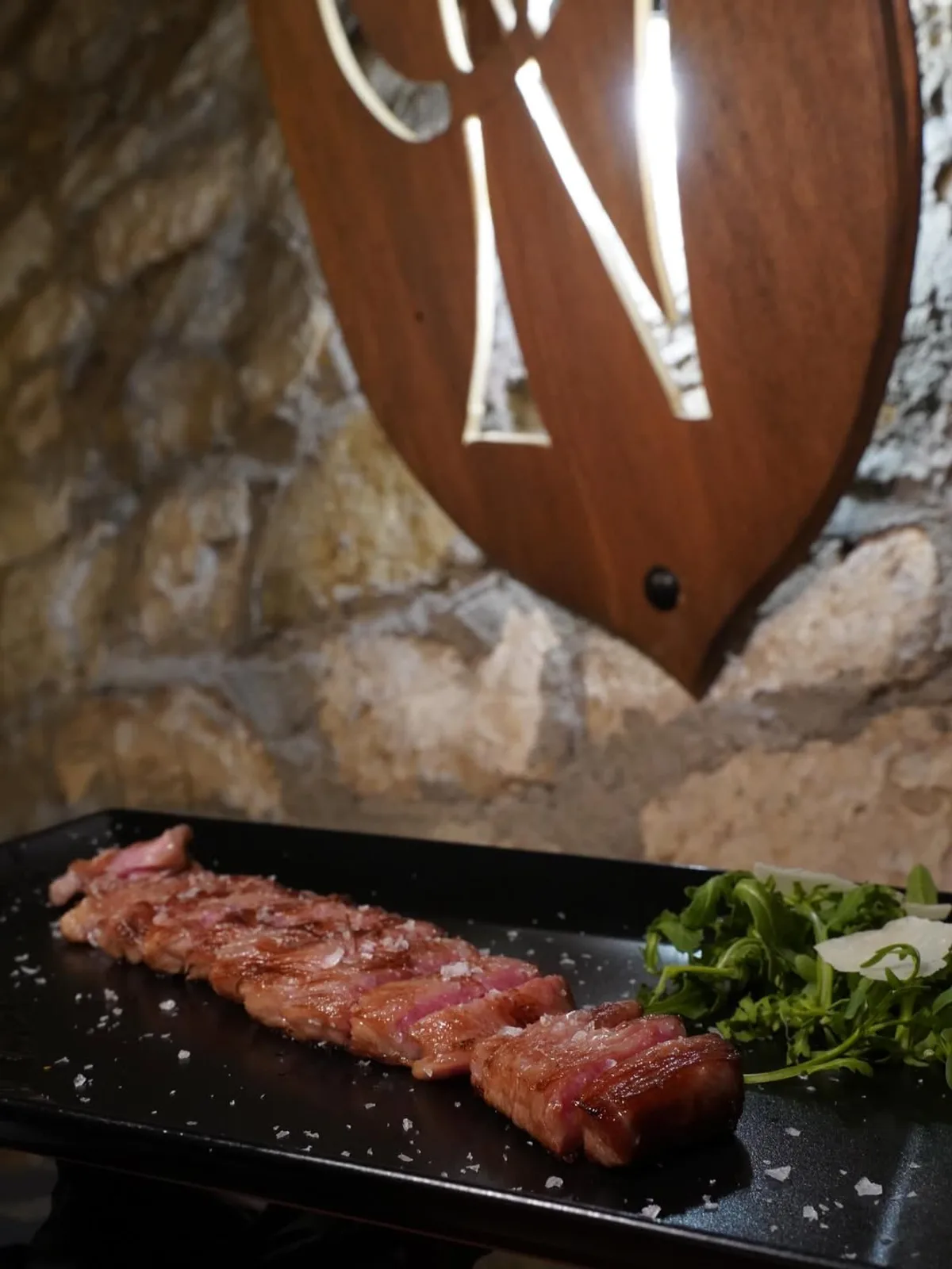 Tagliata alla brace sul vassoio — sullo sfondo le volte in pietra della Grotta dei Priori