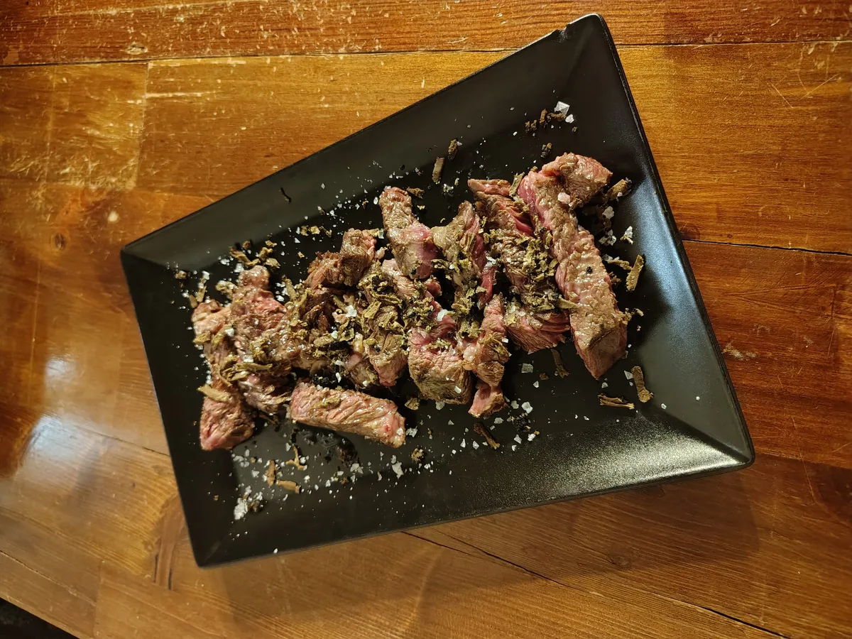 Tagliata di manzo su vassoio nero — carne alla brace con sale in fiocchi e rosmarino