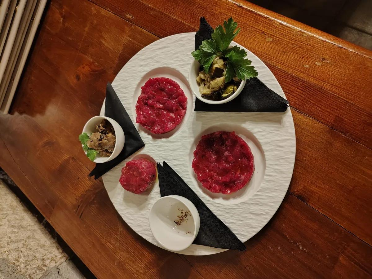 Tartare di Wagyu su piatto rotondo bianco con carpacci, olive e erbe aromatiche